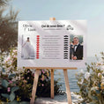 Charger l'image dans la visionneuse de la galerie, Affiche de jeu de mariage “Qui de nous deux ?” installée sur chevalet au bord de l’eau parmi des fleurs.