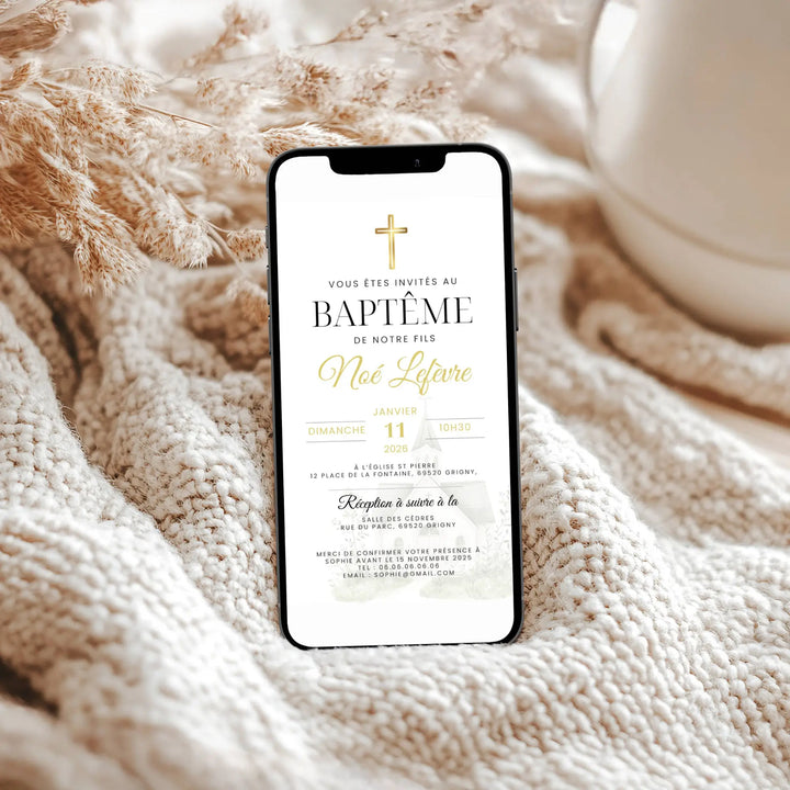 Faire-part digital de baptême affiché sur smartphone, posé sur un plaid beige dans une ambiance cocooning.