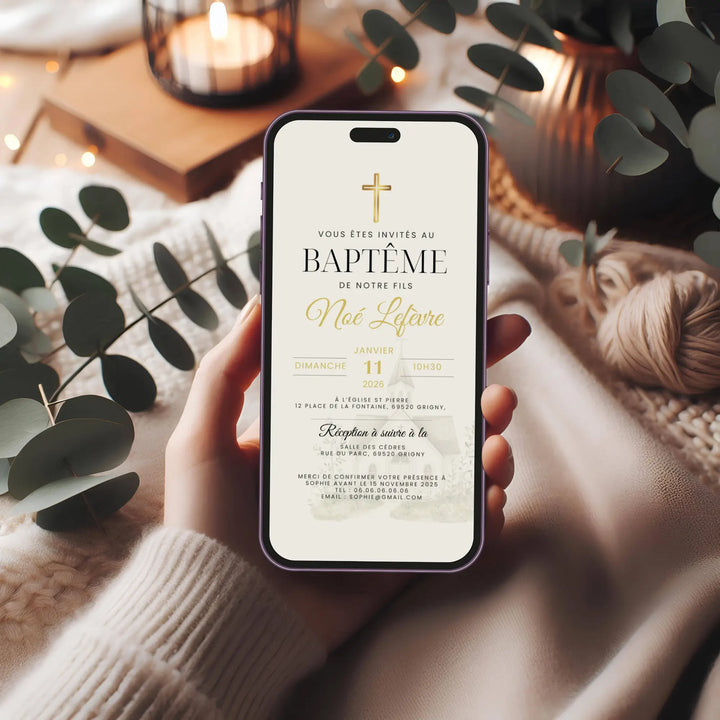 Faire-part de baptême religieux affiché sur smartphone, tenu en main dans une ambiance douce avec feuillage et lumière tamisée.