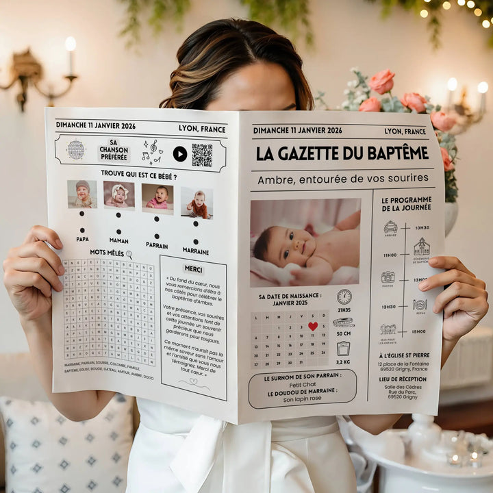 Jeune femme vêtue de blanc tenant devant elle une gazette de baptême moderne personnalisée sur laquelle figure un bébé prénommé Ambre, avec programme de la journée, jeux et photos dans un décor floral élégant.