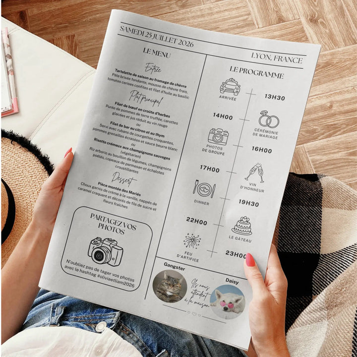 Page intérieure gauche d’une gazette de mariage originale tenue par une personne assise. En haut à gauche, le menu du repas (entrée, plats principaux, dessert). À droite, le programme de la journée illustré avec des icônes : arrivée (13h30), cérémonie de mariage (14h00), photos de groupe (16h00), vin d’honneur (17h00), dîner (19h30), gâteau (22h00), feu d’artifice (23h00). En bas, un encart « Partagez vos photos » avec un appareil photo et un hashtag suivi de deux photos de chats.
