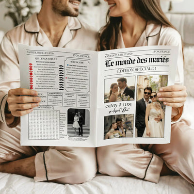 Couple assis en pyjama satin tenant une gazette de mariage originale. La page de gauche contient un quiz, un horoscope, une liste de chansons et une grille de mots mêlés, tandis que la couverture à droite affiche trois photos élégantes des mariés. Les deux personnes sourient en feuilletant le journal.