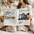Charger l'image dans la visionneuse de la galerie, Couple assis côte à côte en pyjama satiné beige, souriant et feuilletant ensemble une gazette de mariage « Save the Date ».

