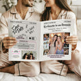 Charger l'image dans la visionneuse de la galerie, Couple assis en pyjamas coordonnés, souriant, tenant ensemble une gazette personnalisée pour demander à une amie d’être témoin de mariage.
