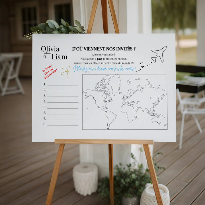 Grande affiche de jeu de mariage “D’où viennent nos invités ?” installée sur un chevalet en bois, avec une carte du monde à compléter et une décoration élégante au thème de mariage.