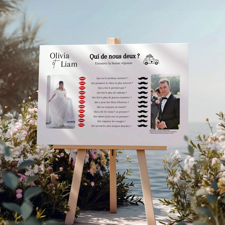 Affiche de jeu de mariage “Qui de nous deux ?” installée sur chevalet au bord de l’eau parmi des fleurs.