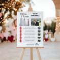 Charger l'image dans la visionneuse de la galerie, Panneau de jeu de mariage “Qui de nous deux ?” personnalisé, affiché sur un chevalet en bois en extérieur décoré de cœurs et guirlandes lumineuses. En haut, deux photos des mariés (madame en robe de mariée, monsieur en smoking). En dessous, une liste de questions amusantes (ex : Qui est le meilleur cuisinier ? Qui dit “je t’aime” en premier ?) avec, à gauche, des icônes de lèvres rouges symbolisant la mariée et à droite des moustaches noires symbolisant le marié, pour voter. 
