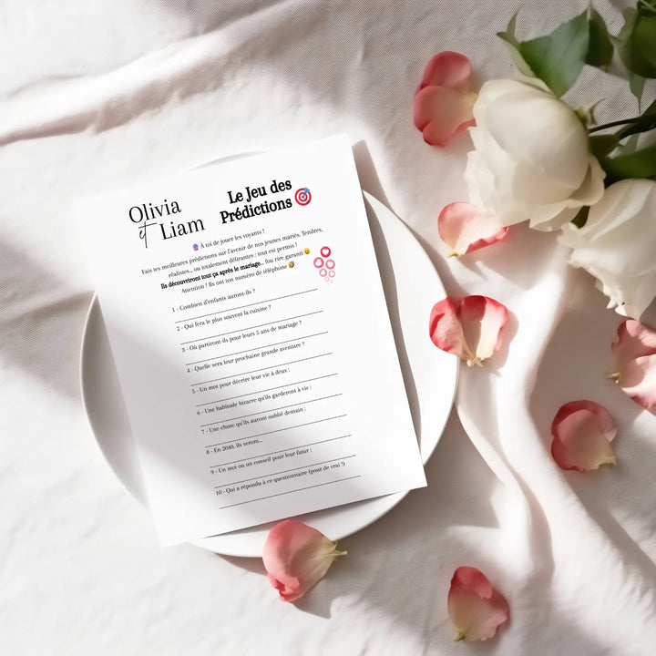 Fiche de jeu de mariage “Le jeu des prédictions” posée dans une assiette entourée de pétales de roses, mise en scène sur une table élégante.