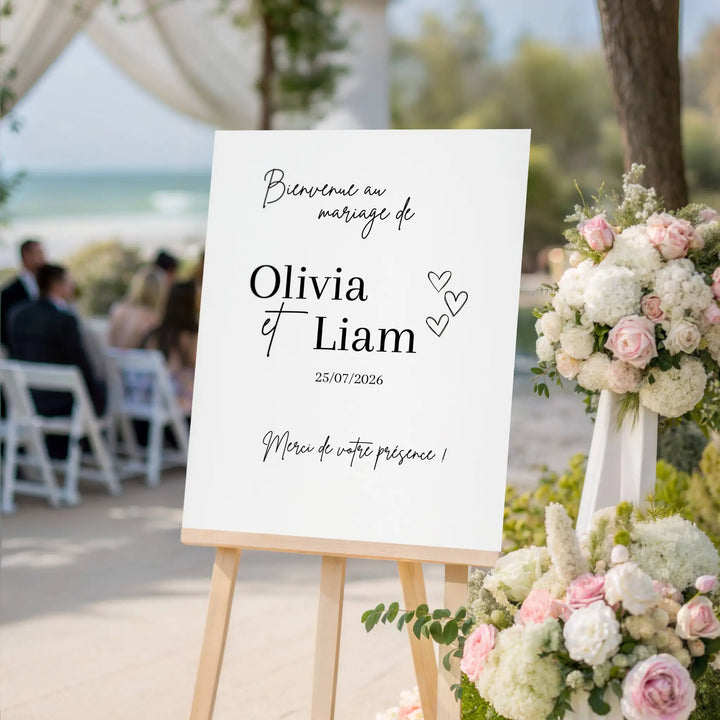 Panneau de bienvenue mariage personnalisé avec prénoms et date. Exemple Olivia et Liam, affiche élégante sur chevalet entourée de fleurs et bouquet de roses. 