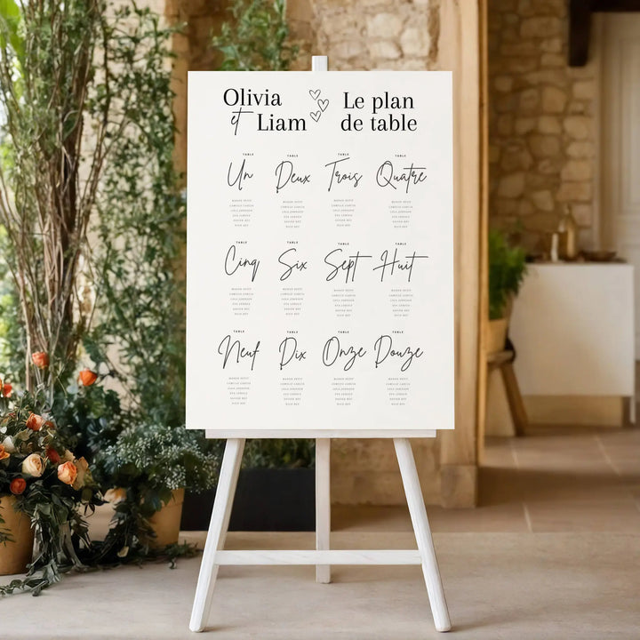 Plan de table mariage élégant sur chevalet, affiche personnalisée avec prénoms des mariés et numéros de table, décoration de réception chic avec fleurs.
